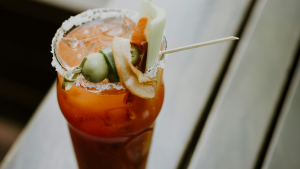 Close up photo of a Bloody Mary cocktail. The rim is dipped in salt and there is a skewer with olives, jalapeños, and celery.