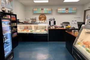 Interior photo of Sierra Gold Seafood market. There is freezer of a variety of products, a shelve of food sauces, and a display case of fish.