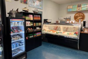 Interior photo of Sierra Gold Seafood market. There is freezer of a variety of products, a shelve of food sauces, and a display case of fish.